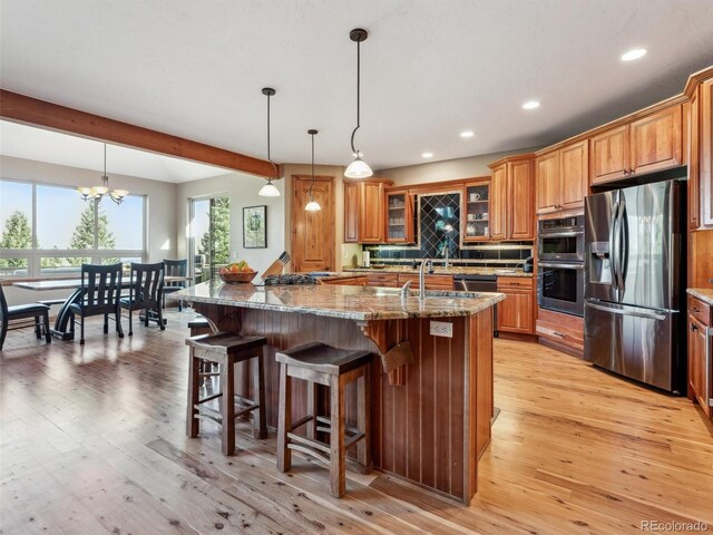 kitchen featuring a breakfast bar, light wood-type flooring, beam ceiling, brown cabinets, and stainless steel appliances