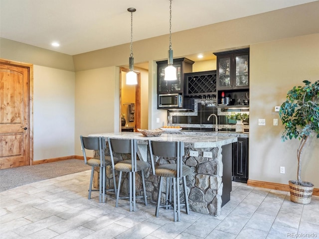 kitchen with pendant lighting, light stone counters, stainless steel microwave, a kitchen breakfast bar, and a kitchen island