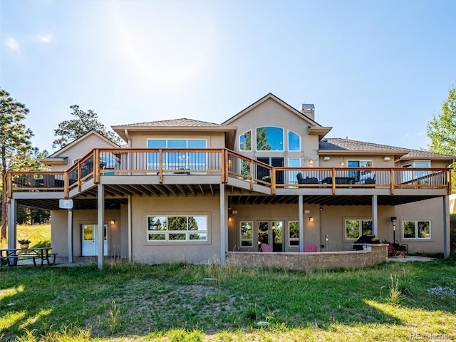 back of property with stucco siding, a yard, a deck, and a chimney