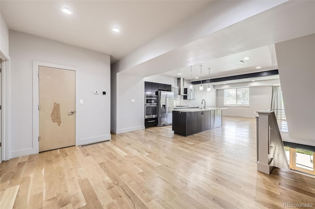 kitchen featuring a center island with sink, pendant lighting, stainless steel appliances, and light hardwood / wood-style flooring