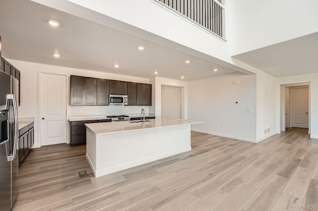 kitchen featuring a center island with sink, light countertops, dark brown cabinetry, light wood-style floors, and appliances with stainless steel finishes