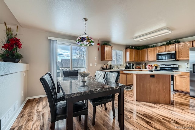 kitchen featuring appliances with stainless steel finishes, hanging light fixtures, light hardwood / wood-style floors, a center island, and sink