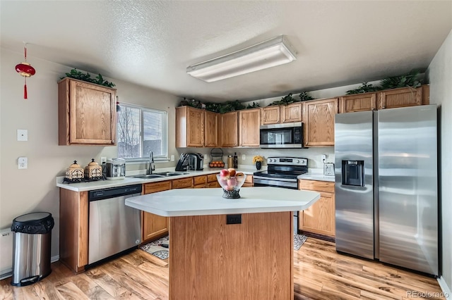 kitchen with a textured ceiling, light hardwood / wood-style flooring, stainless steel appliances, a kitchen island, and sink