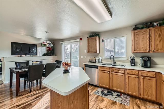 kitchen featuring stainless steel dishwasher, a center island, hanging light fixtures, light wood-type flooring, and sink