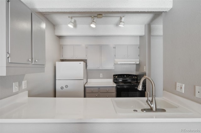 kitchen featuring black electric range, light countertops, freestanding refrigerator, a sink, and under cabinet range hood