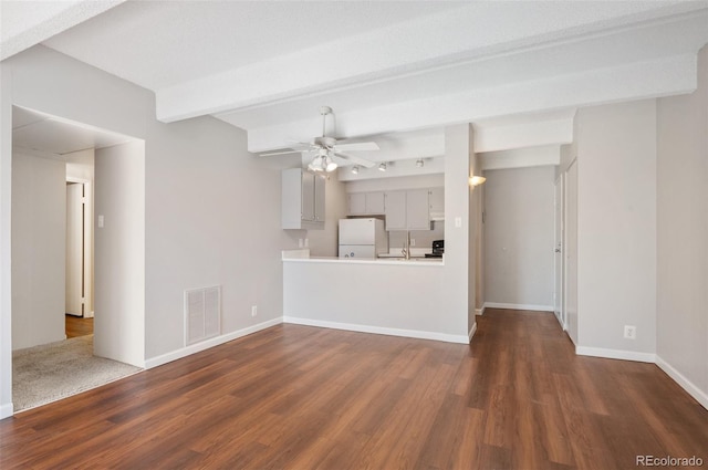 unfurnished living room featuring dark wood-type flooring, visible vents, baseboards, a ceiling fan, and beam ceiling