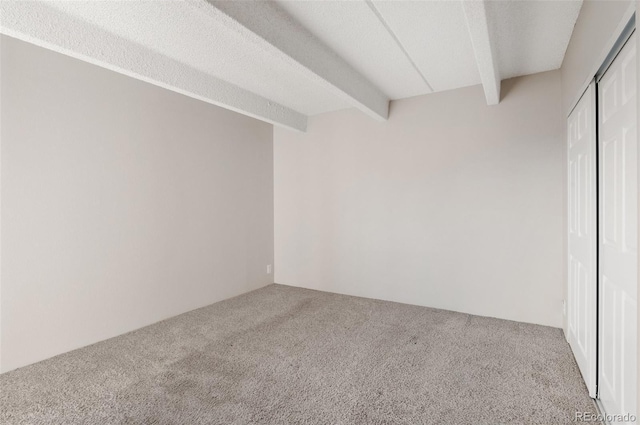 carpeted spare room featuring a textured ceiling and beam ceiling