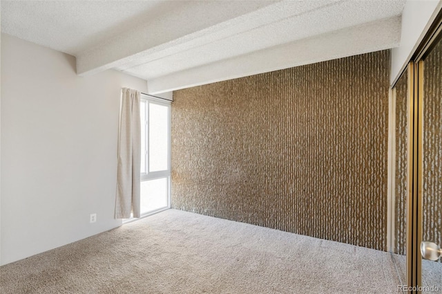 unfurnished room with carpet floors, beam ceiling, and a textured ceiling