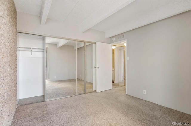 unfurnished bedroom featuring a textured ceiling, beamed ceiling, and carpet flooring