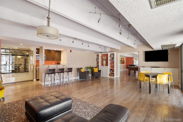 living room featuring track lighting, baseboards, wood finished floors, a textured ceiling, and beam ceiling