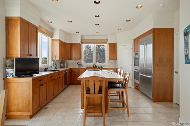 kitchen featuring sink, backsplash, a kitchen island with sink, a breakfast bar, and appliances with stainless steel finishes