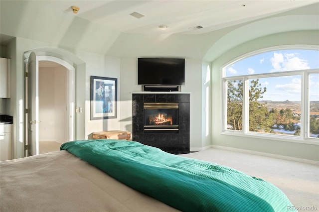 carpeted bedroom featuring vaulted ceiling, multiple windows, and a tiled fireplace