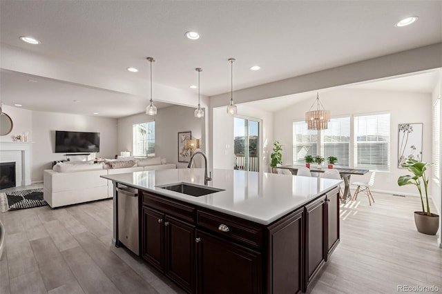 kitchen with decorative light fixtures, dishwasher, sink, a kitchen island with sink, and light hardwood / wood-style flooring