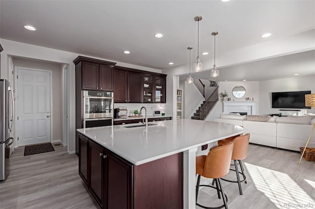 kitchen with appliances with stainless steel finishes, decorative light fixtures, sink, a kitchen island with sink, and dark brown cabinets