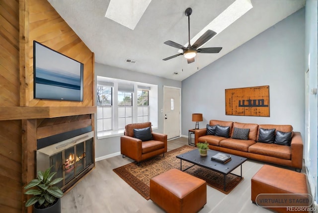 living room featuring light wood-type flooring, a skylight, ceiling fan, high vaulted ceiling, and wood walls