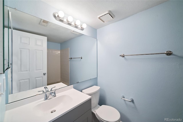 bathroom with vanity, toilet, a tile shower, and a textured ceiling