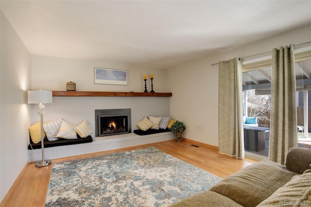 living area featuring visible vents, a fireplace, baseboards, and wood finished floors