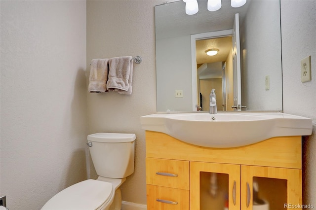 half bath with vanity, toilet, and a textured wall