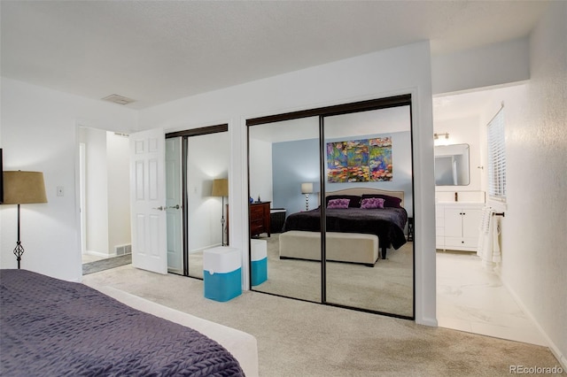 carpeted bedroom featuring visible vents, multiple closets, and connected bathroom