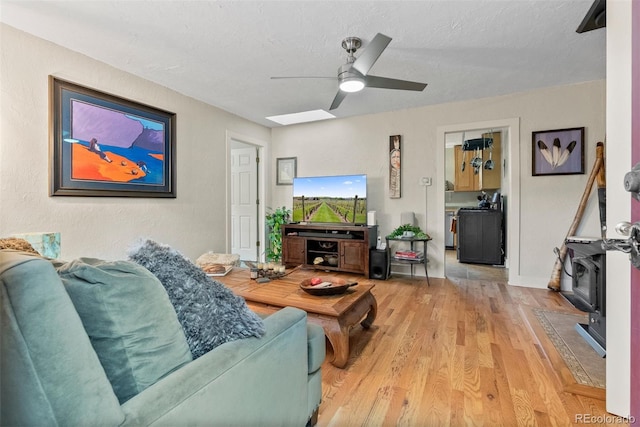 2874 SE Grapevine Rd, Idledale, CO 80453 - living room with light wood-style flooring, a ceiling fan, a wood stove, and a skylight