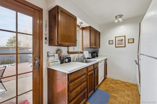 kitchen with brown cabinets, light countertops, a sink, white appliances, and baseboards