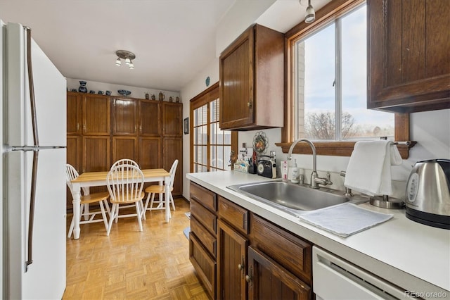 kitchen with light countertops, a sink, freestanding refrigerator, and dishwashing machine