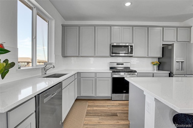 8728 Hotchkiss St, Littleton, CO 80125 - kitchen with stainless steel appliances, a sink, gray cabinetry, light wood finished floors, and light stone countertops