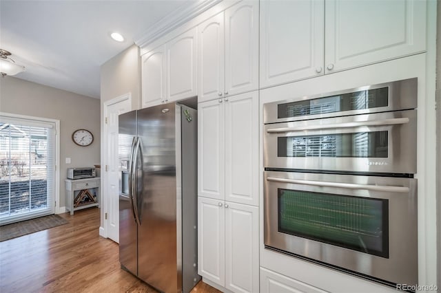 kitchen with light wood finished floors, stainless steel appliances, recessed lighting, white cabinets, and baseboards