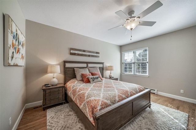 bedroom featuring baseboards, a baseboard heating unit, ceiling fan, and wood finished floors