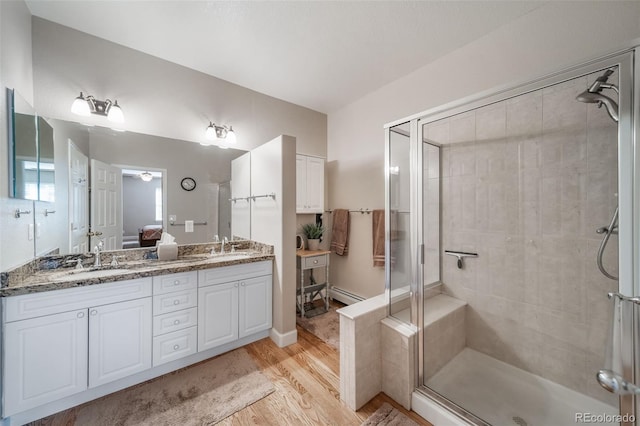 full bathroom with a baseboard heating unit, wood finished floors, a sink, double vanity, and a stall shower