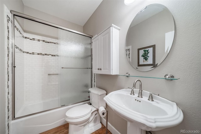 full bath featuring enclosed tub / shower combo, a textured wall, a sink, and toilet