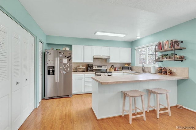 387 Upham St, Lakewood, CO 80226 - kitchen with appliances with stainless steel finishes, under cabinet range hood, light wood-style floors, light countertops, and a peninsula