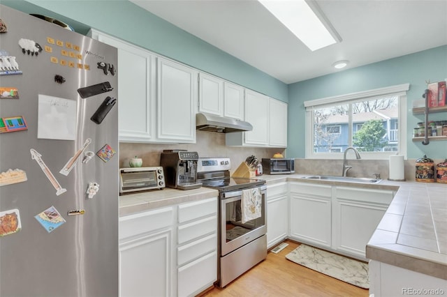 387 Upham St, Lakewood, CO 80226 - kitchen featuring stainless steel appliances, a sink, under cabinet range hood, tile countertops, and white cabinetry