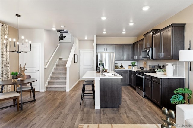 kitchen featuring stainless steel appliances, dark brown cabinets, a breakfast bar area, wood finished floors, and a sink