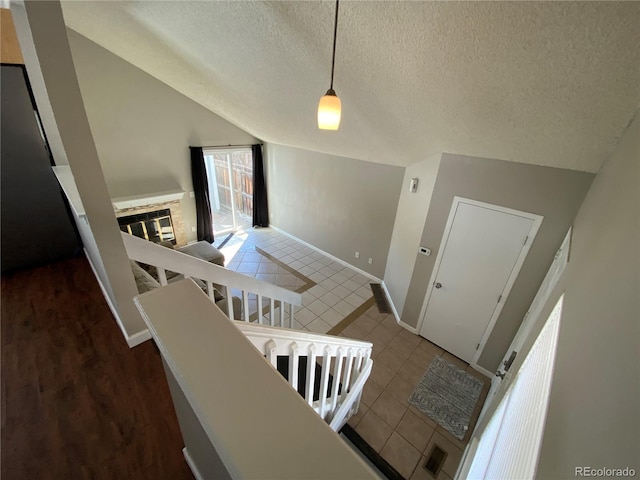 staircase featuring vaulted ceiling, a glass covered fireplace, a textured ceiling, tile patterned flooring, and baseboards