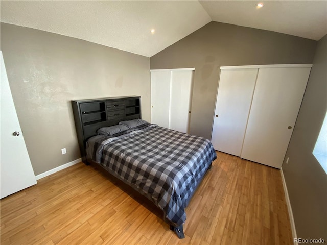 bedroom with baseboards, lofted ceiling, light wood-style floors, and two closets
