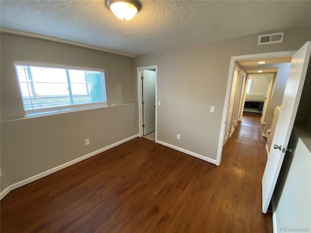 unfurnished bedroom featuring dark wood-style flooring, a textured ceiling, baseboards, and visible vents