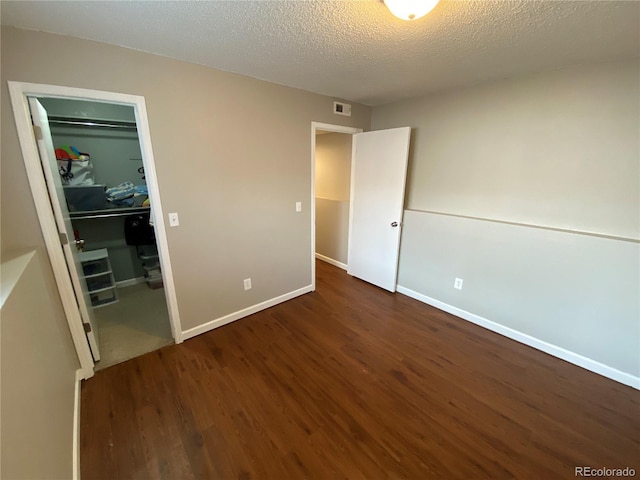 unfurnished bedroom featuring a closet, wood finished floors, a spacious closet, a textured ceiling, and visible vents
