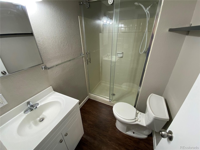 bathroom featuring toilet, wood finished floors, vanity, a stall shower, and a textured wall