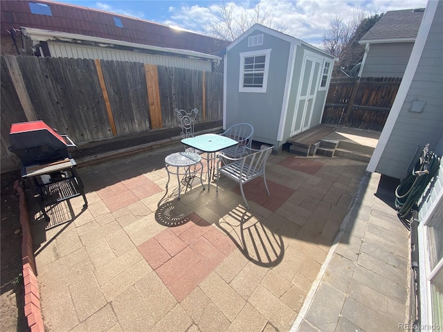 view of patio / terrace with a fenced backyard, an outbuilding, outdoor dining area, and a storage shed