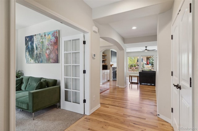 hallway with arched walkways, light wood finished floors, baseboards, and recessed lighting