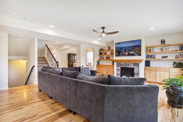 living room featuring arched walkways, a fireplace, light wood-type flooring, ceiling fan, and stairs