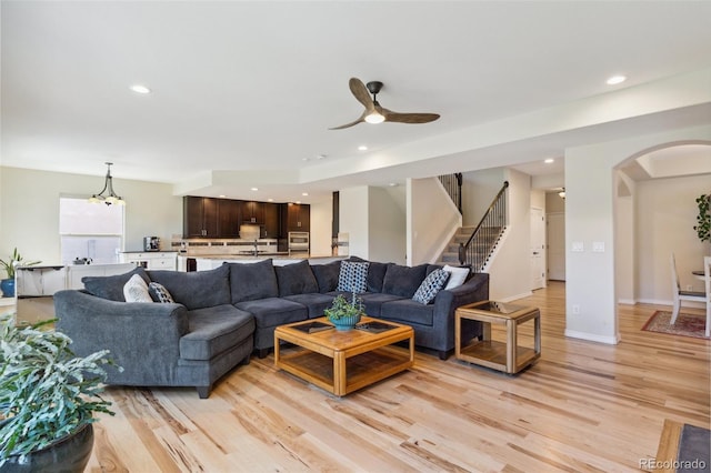 living area with arched walkways, ceiling fan, light wood-style floors, recessed lighting, and stairway