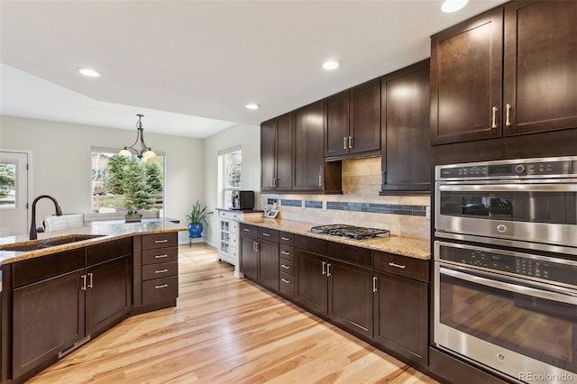 kitchen with appliances with stainless steel finishes, a sink, light wood-type flooring, light stone counters, and recessed lighting
