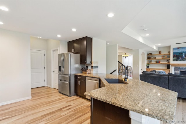 kitchen featuring stainless steel appliances, a sink, light wood-type flooring, dark brown cabinetry, and light stone countertops