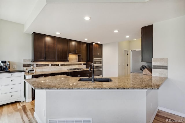 kitchen featuring a sink, stainless steel gas stovetop, dark brown cabinets, light stone counters, and a peninsula