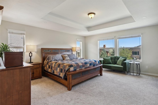 bedroom with light carpet, a tray ceiling, and baseboards