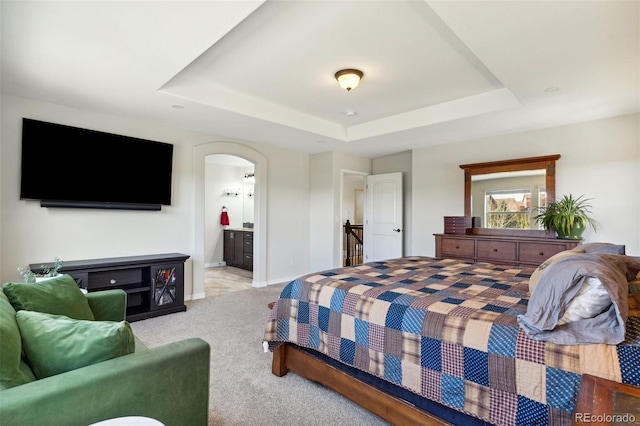 bedroom featuring a raised ceiling, light carpet, arched walkways, connected bathroom, and baseboards