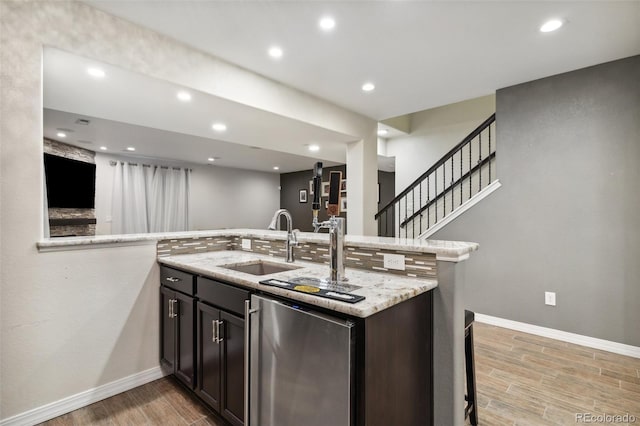 kitchen with a sink, refrigerator, light wood-style floors, baseboards, and light stone countertops