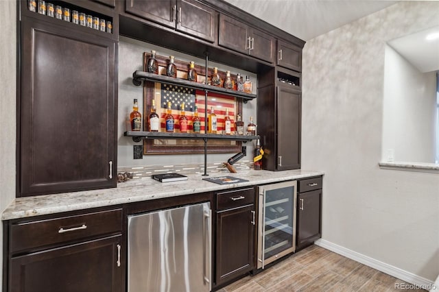 indoor wet bar with fridge, beverage cooler, baseboards, and light wood-style flooring